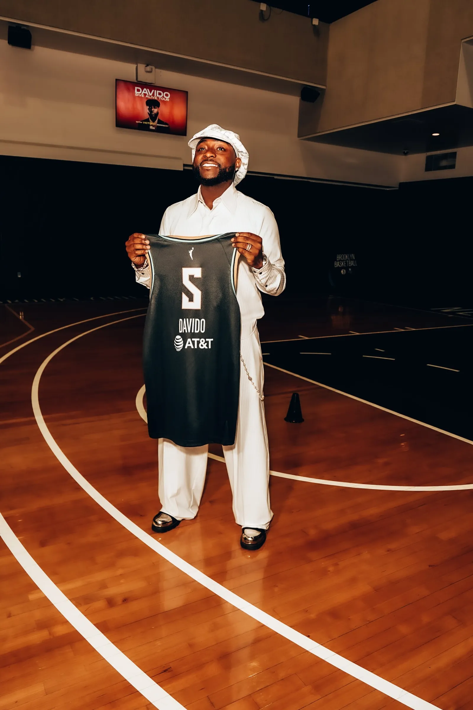 Davido holding a custom New York Liberty jersey on a Brooklyn basketball court