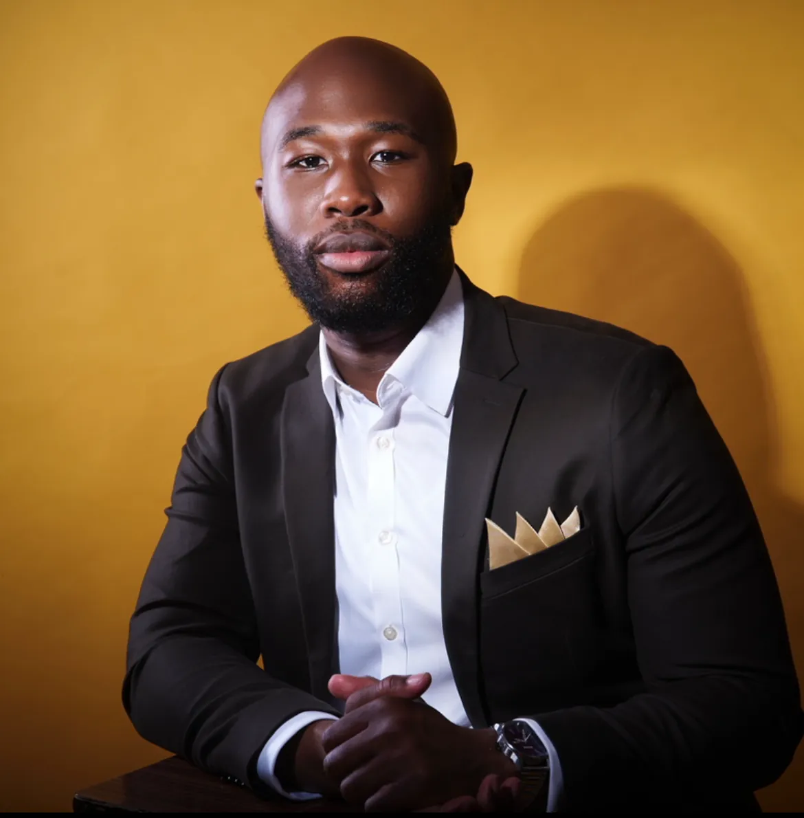 Idia Ogala, founder of CBG Creators, in a black suit against a gold wall